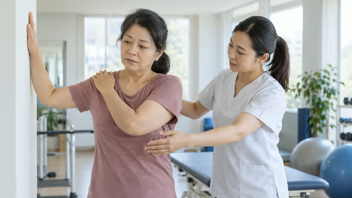 Người bệnh đau vai được nhân viên phục hồi chức năng hỗ trợ vận động