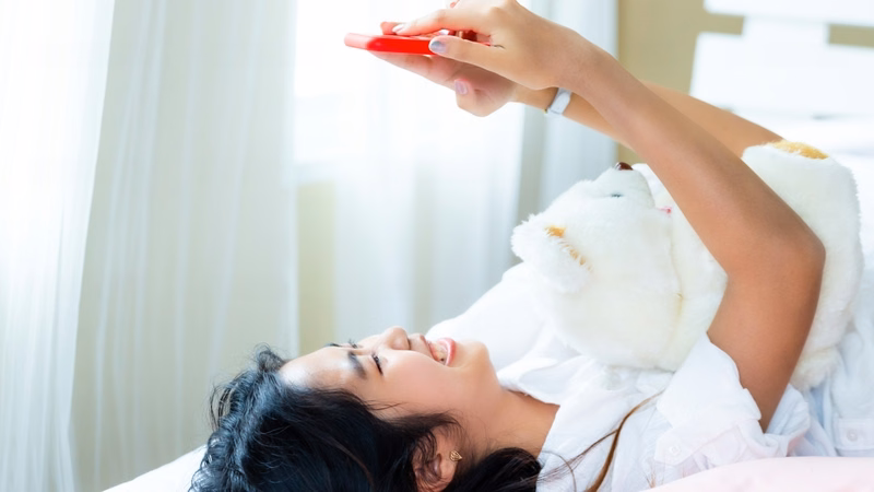 Người nằm nghỉ trên giường lướt điện thoại để thư giãn sau giờ làm việc căng thẳng